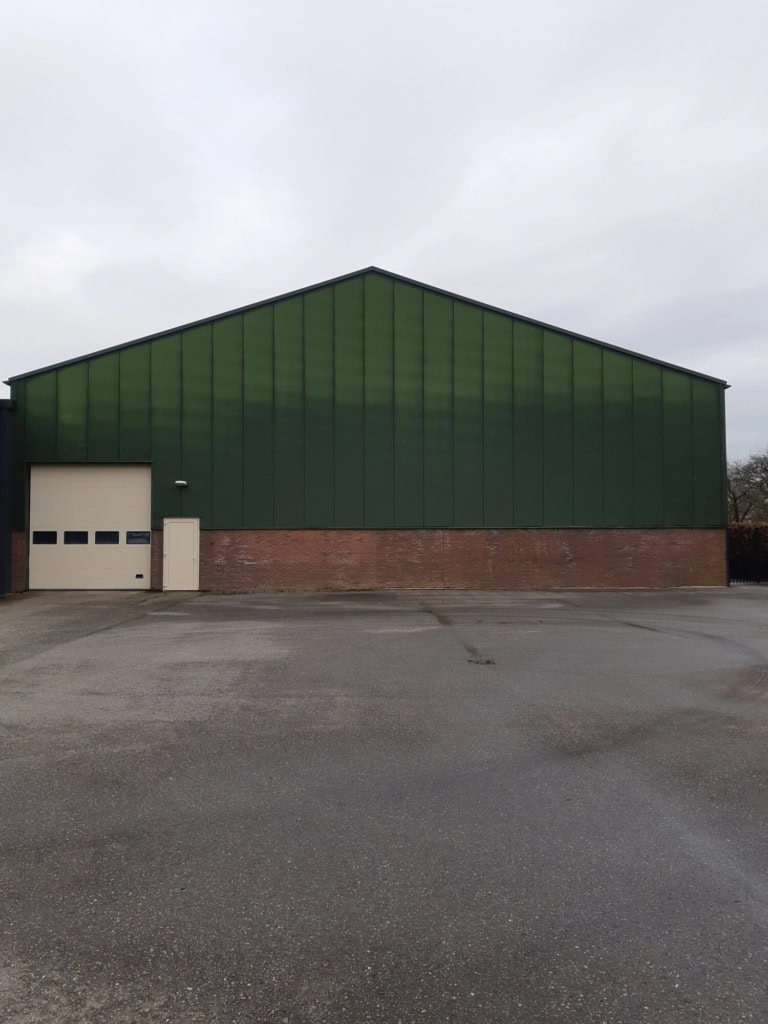 Groene bedrijfshal met garagepoort en brick onderkant.