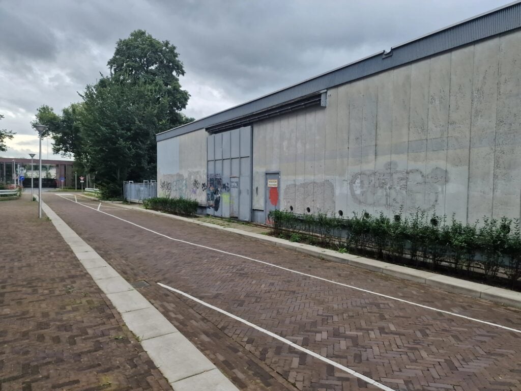 Industriële gevel van een bouwbedrijf met graffiti en planten.