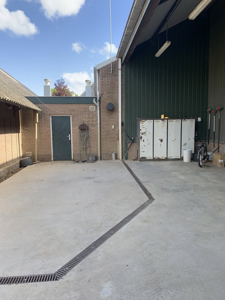 Buitenruimte met betonvloer en afwatering door drainagegoot.