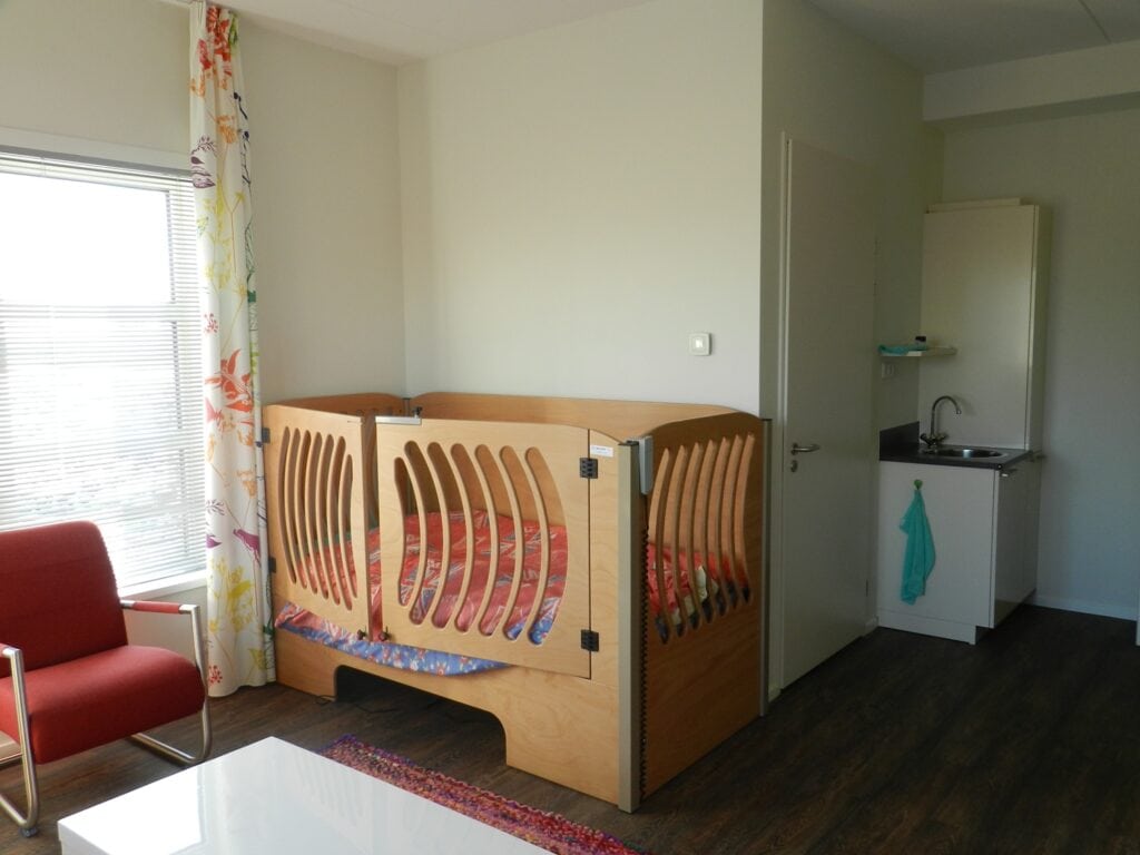 Kinderbed in lichte woonkamer met grote ramen en kleurrijke gordijnen.
