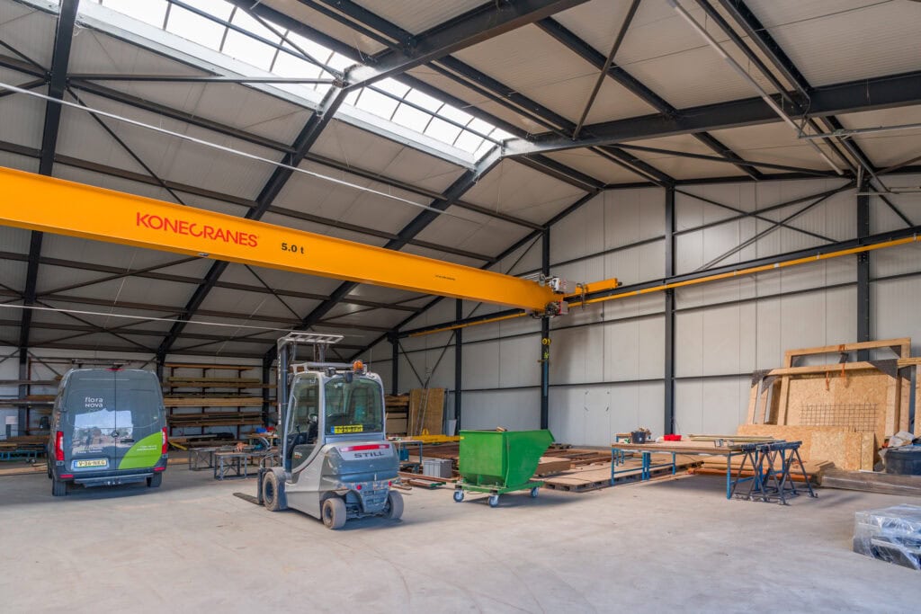 Bouwbedrijfshal met hijskraan, heftruck en bouwmaterialen.