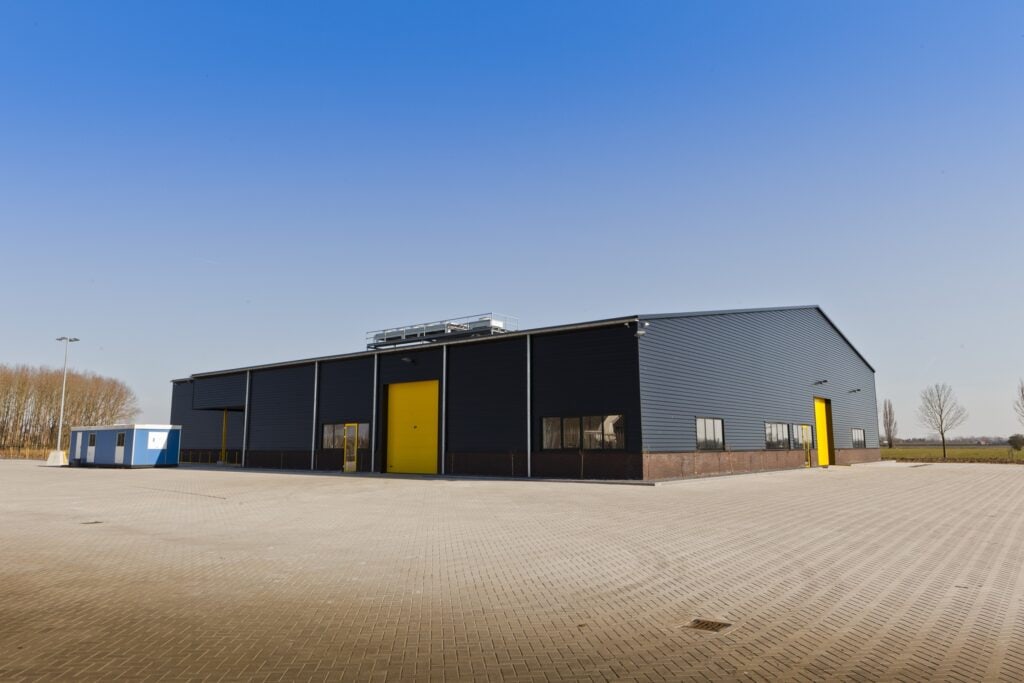 Moderne bedrijfsloods met zwarte gevel en gele deuren in open veld.