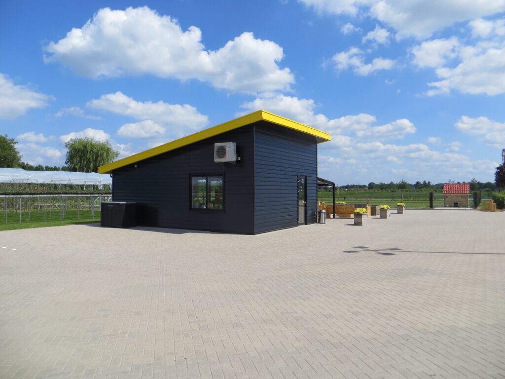 Moderne zwarte bouwcontainer met gele dakrand op een open terrein.