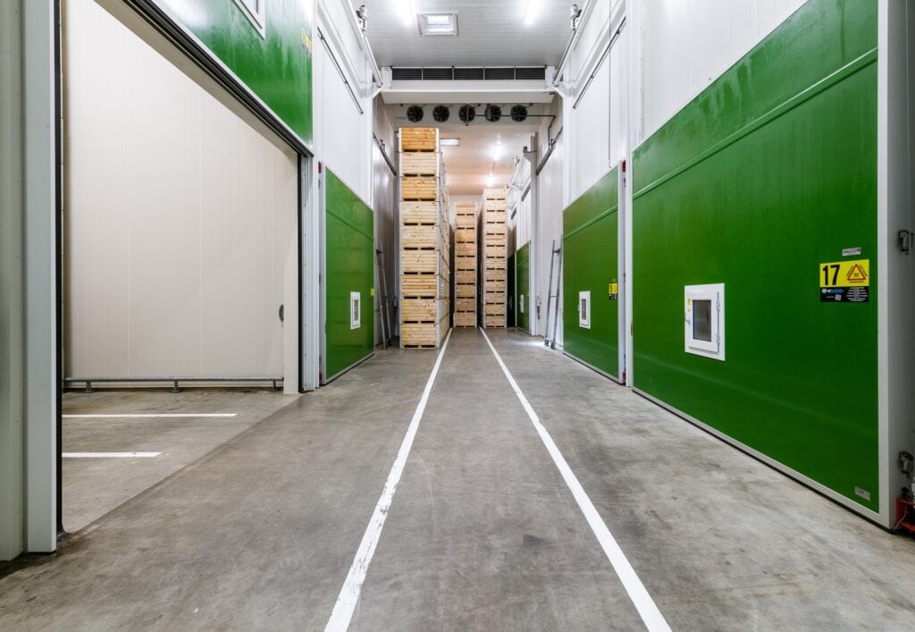 Binnenkant van een opslagruimte met houten pallets en groene muren.