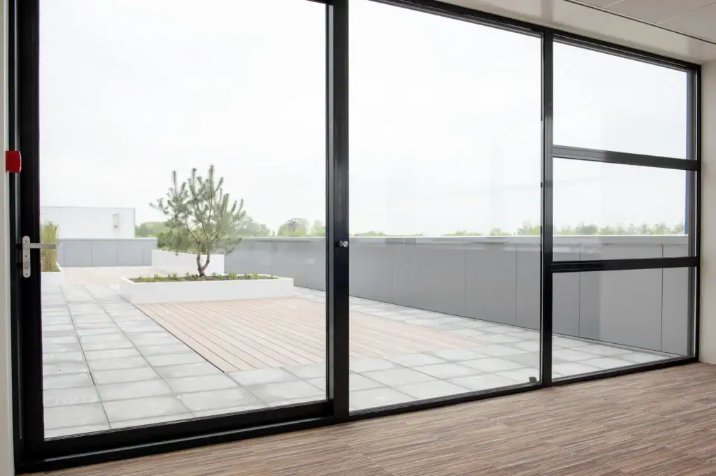 Grote glazen schuifdeuren die uitkijken op terras en tuin.
