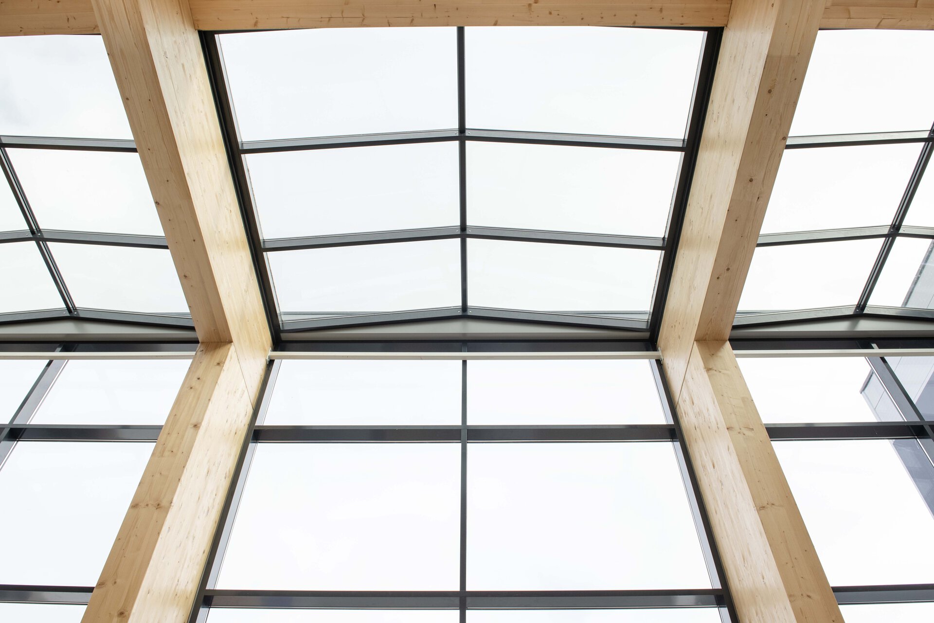 Hoog plafond met houten liggers en glazen dakramen.
