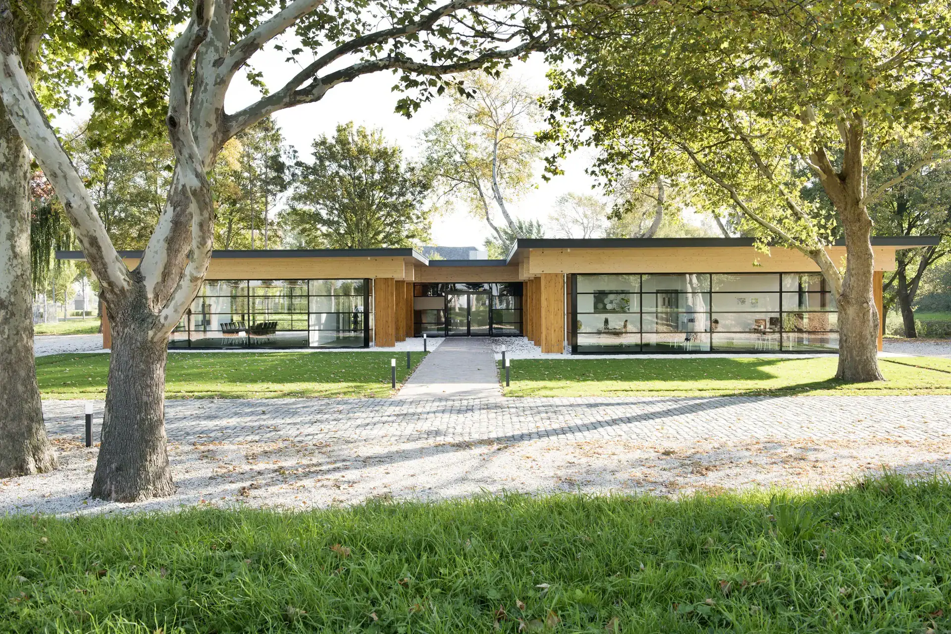 Moderne houten gebouw met grote ramen, omgeven door bomen, strak landschapsontwerp.
